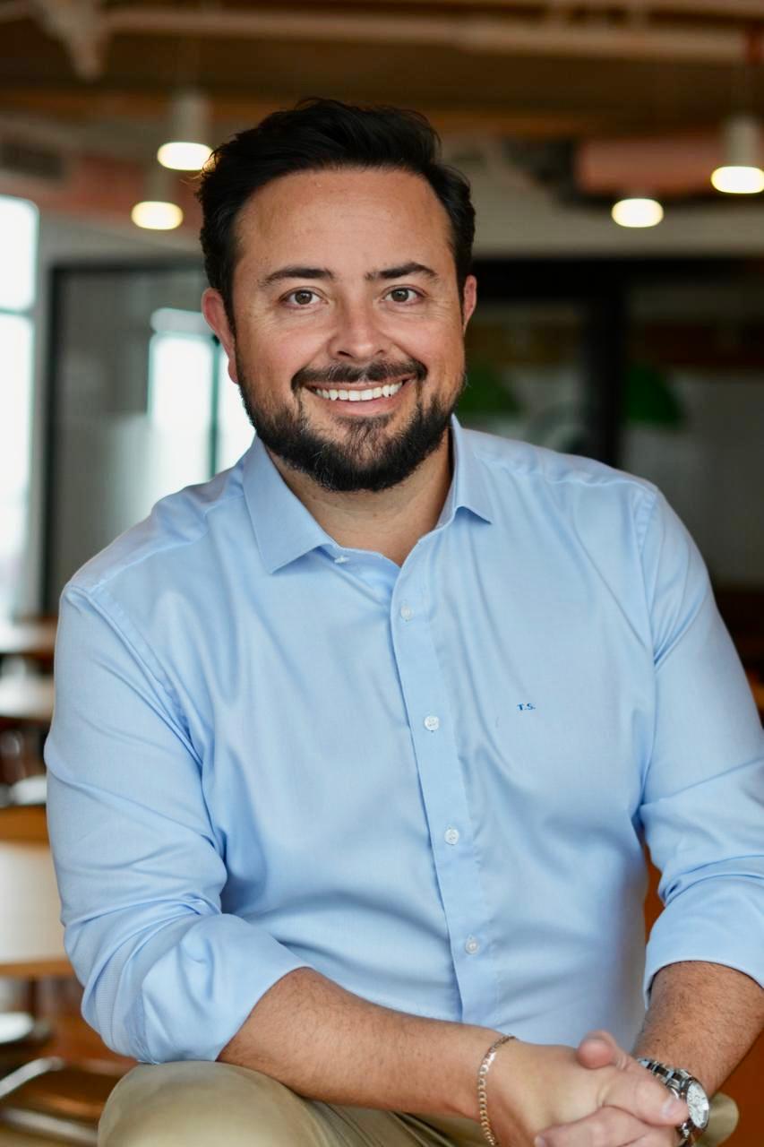 Retrato de Tiago Stachon, de camisa azul-clara, sentado em um ambiente profissional